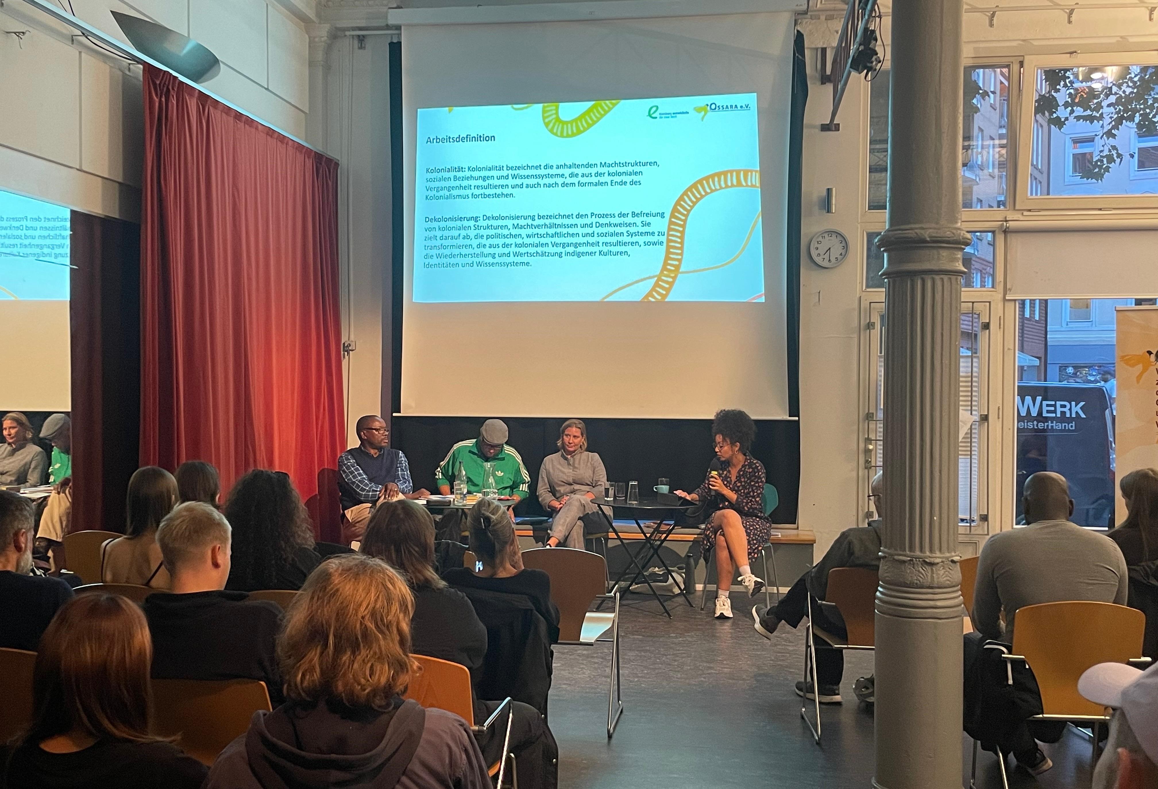 Bild vom Panel von links nach rechts: Simon, Daniel, Nadja, Kalina. Im Hintergrund eine PowerPoint Präsentation an die Wand ausgestrahlt.