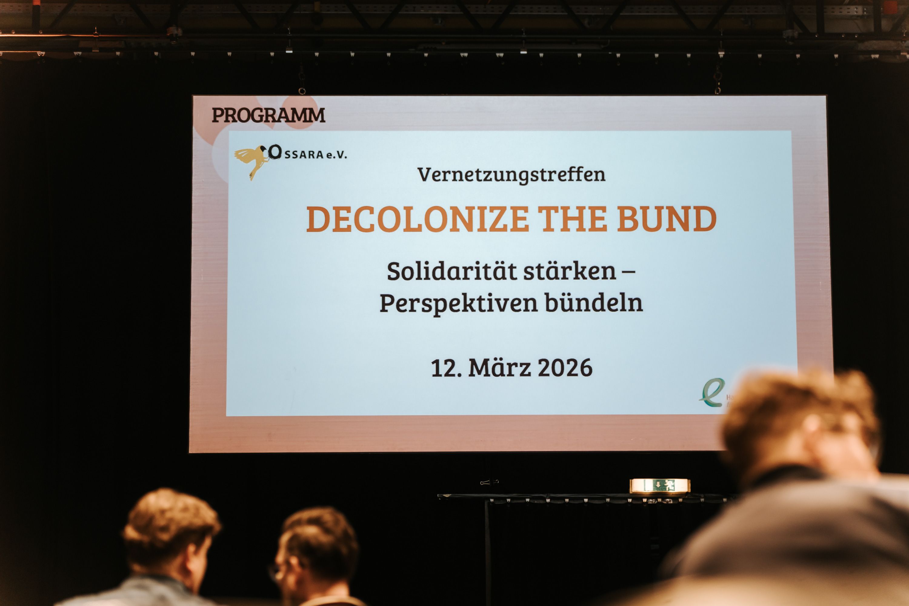 Folie auf einer Bühne mit dem Titel ‚Decolonize the Bund – Solidarität stärken, Perspektiven bündeln‘, gezeigt bei einem Vernetzungstreffen von Ossara e.V. (12. März 2026).